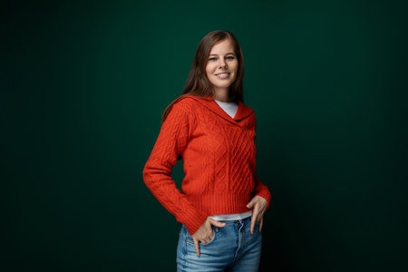 Beautiful slim woman with brown hair dressed in a red sweater and jeans on a green backgroundの写真素材