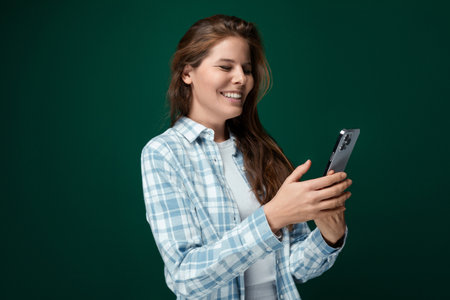 A young woman with brown hair wears a checkered blue shirt and stands on a green background with copy spaceの写真素材