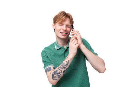 young caucasian man with red hair dressed in a green t-shirt speaks on the phone against the background with copy spaceの写真素材