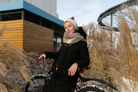 Young woman dressed warmly with scarf and headband rides a bicycle in winterの写真素材