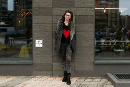 Street fashion concept, young European woman with dreadlocks wearing a dark jacket in an urban...