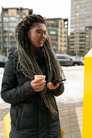 Photo on the street, young pretty informal woman with dreadlocks hairstyle smiling sweetly