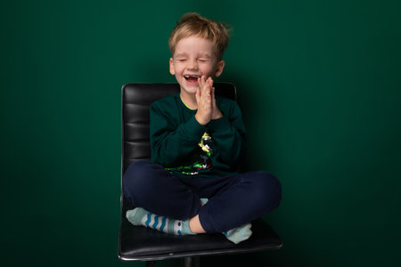 European blond boy dressed casually posing while sitting on a chair on a green backgroundの写真素材