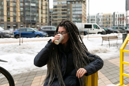 Lifestyle concept, young European woman with informal dreadlocks hairstyle drinks coffee while...
