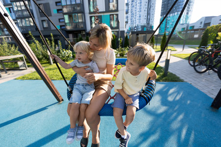 Mother Enjoying Quality Time With Her Two Sons at a Playground Swinging Together on a Sunny Dayの写真素材