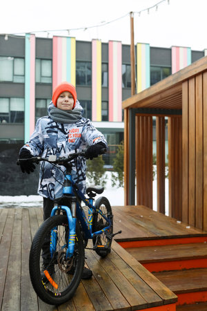 A Caucasian boy dressed in a winter jacket walks with a bicycle around the cityの写真素材