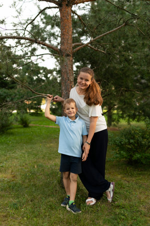 A joyful moment shared between a mother and son in a peaceful park during a sunny afternoon, standing beside a tall treeの写真素材
