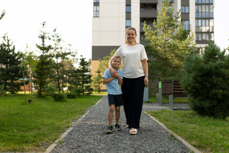 Mother and son enjoy a sunny day while walking together in a park filled with greenery and a clear blue skyの写真素材
