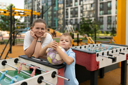 A joyful moment shared between a mother and son at a city playground, enjoying foosball and soccer on a sunny afternoonの写真素材