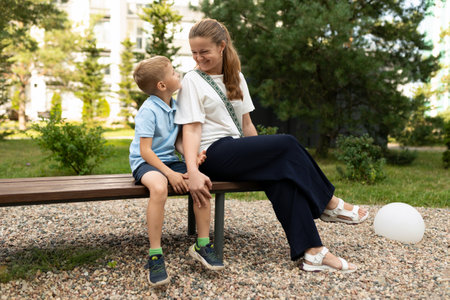 A joyful moment between a mother and her son sitting on a bench in a park, sharing smiles and laughter on a sunny afternoonの写真素材