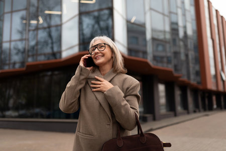 Senior businesswoman talking on the phone outside a modern office building in an urban environment during the afternoonの写真素材