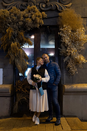 A couple walks hand-in-hand through the city at night, stopping for a moment to look at something in a shop windowの写真素材