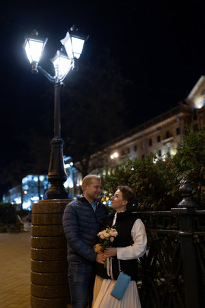 A couple strolls through the city at night, illuminated by a streetlampの写真素材