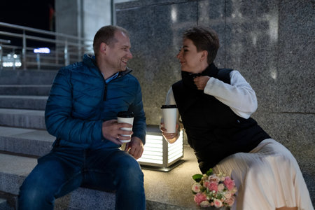 A couple enjoys a night out in the city, taking a moment to sit and talk on a set of stepsの写真素材