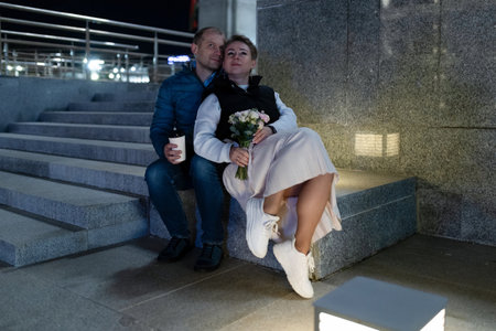 A couple sits together on a set of stairs in the city at nightの写真素材