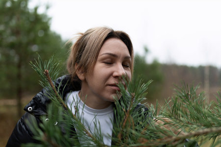 A woman enjoys the fresh scent of pine branches while exploring a tranquil forest during an overcast day in early autumnの写真素材