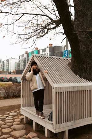 Person standing in a wooden house structure near a tree on a cloudy day in an urban environment
