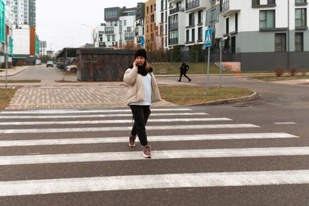 Person crossing a pedestrian walkway in a modern urban neighborhood during overcast weatherの写真素材