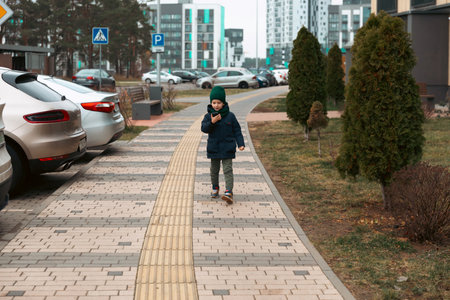 Child walking on a sidewalk in a modern urban area while using a smartphoneの写真素材