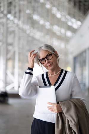 A middle-aged businesswoman reflects thoughtfully while holding a tablet during the afternoonの写真素材