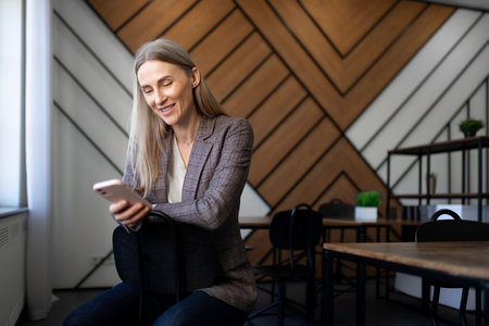 Woman enjoying a moment of leisure while using a smartphone in a modern cafe setting with stylish wooden decorの写真素材