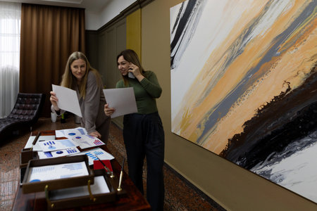 Two women collaborating on design project in modern workspace with abstract art on wall