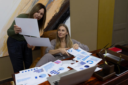 Two women reviewing data charts during a business meeting in a modern office settingの写真素材