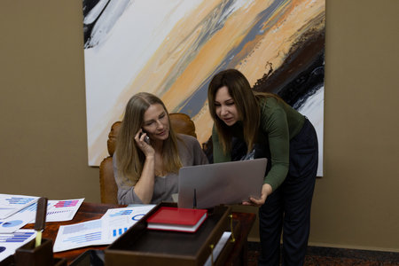 Women collaborating in an office setting, discussing a laptop while reviewing business documents and chartsの写真素材