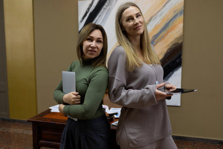 Two women pose confidently in an office setting while engaged in a professional discussion during a workdayの写真素材