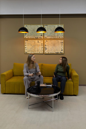 Two women engage in conversation while sitting on a yellow couch in a stylish interior setting with decorative maps on the wallの写真素材