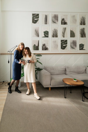 Two women collaborating in a modern living room, sharing ideas and enjoying coffee while standing togetherの写真素材