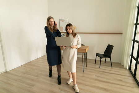Two women collaborating in a modern workspace while reviewing a laptop togetherの写真素材