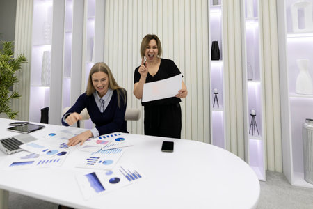 Colleagues celebrate success during a project review in a modern office space with charts and graphs on displayの写真素材