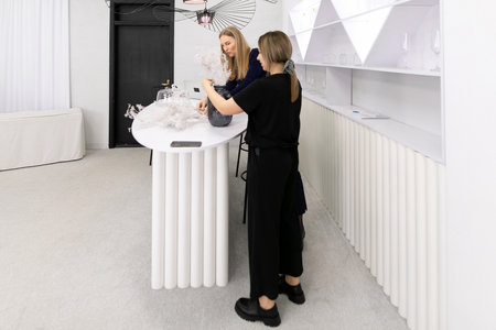 Two women work together at a modern bar setting, preparing floral arrangements in a contemporary interior spaceの写真素材
