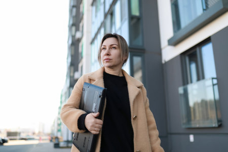 Woman walks confidently with laptop in an urban setting during the dayの写真素材