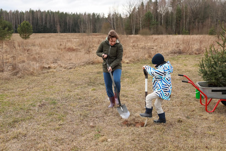 Woman and child planting a tree in a field during early spring in a peaceful rural settingの写真素材
