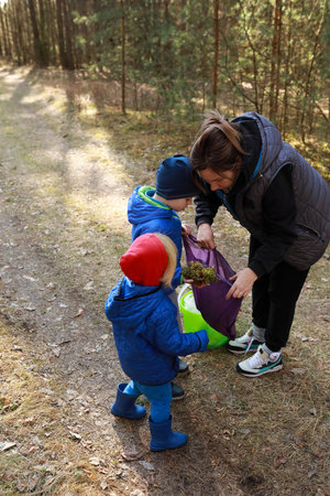 Two children help their mother collect plants while exploring a forested trailの写真素材