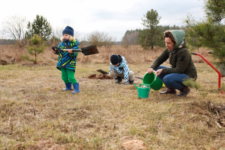Children and adult planting trees in a grassy field on a cloudy dayの写真素材