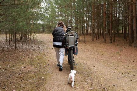 Woman walks with child on bicycle in forest while dog runs alongside them during a sunny afternoon outingの写真素材