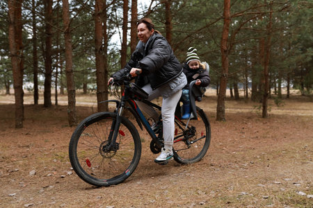 Parent and child enjoy a bike ride through a tranquil forest in autumn near a serene path surrounded by natureの写真素材