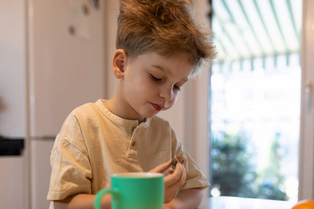 Child enjoys snack at home while sitting at the kitchen table on a sunny afternoonの写真素材