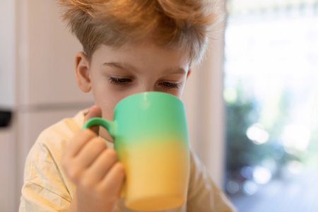 Young child enjoys a colorful mug of beverage while sitting at home in daytimeの写真素材