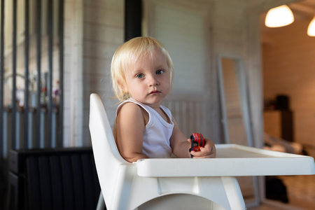 Child in high chair playing with toy car in cozy indoor setting during daylightの写真素材