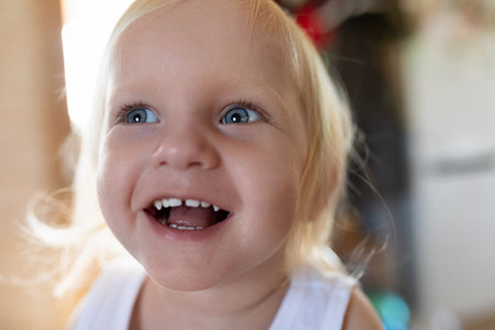 Cheerful child with bright blue eyes smiling joyfully in a cozy indoor setting during day timeの写真素材