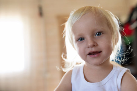 Child with light blonde hair smiling in a cozy indoor setting during daylight hours, capturing innocence and joy of childhoodの写真素材