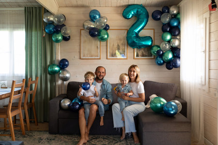Family celebration featuring two children with balloons in a cozy living room during a joyful birthday partyの写真素材