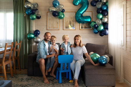 Family celebrates second birthday with balloons and decorations in cozy living roomの写真素材