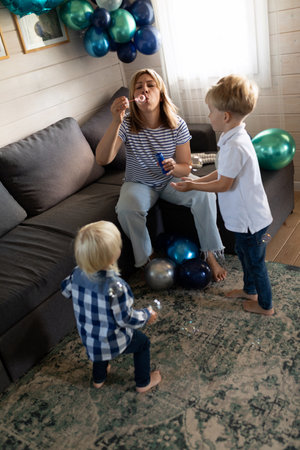 Family celebration at home with children enjoying bubble fun on a cozy couch surrounded by colorful balloonsの写真素材