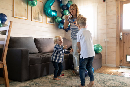 Kids enjoying bubble play indoors during a festive family gathering in a cozy living room decorated with balloonsの写真素材