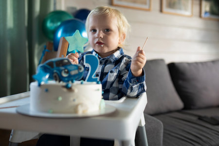 Celebration of a second birthday with a child enjoying cake and decorations in a cozy interior settingの写真素材